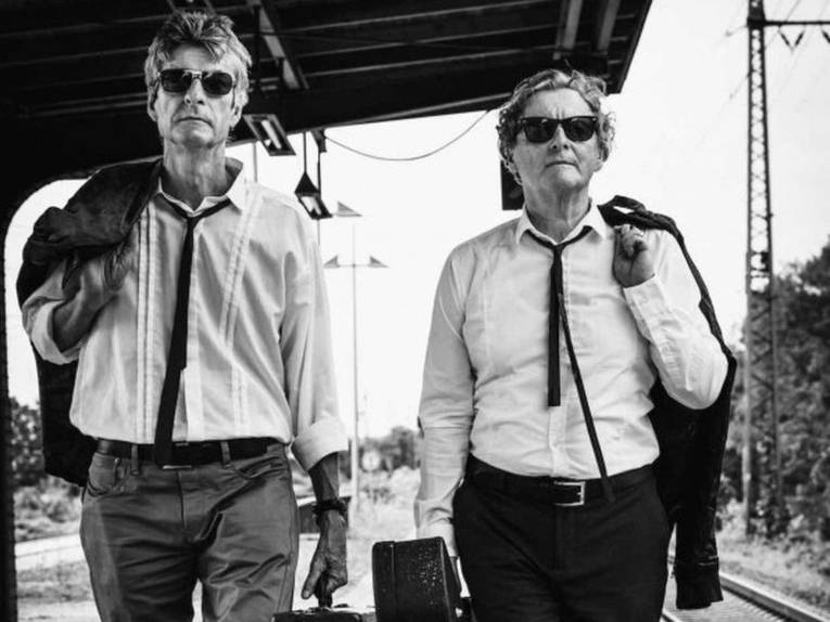 Zwei Männer mit Instrumentenkoffern auf einem Bahnsteig